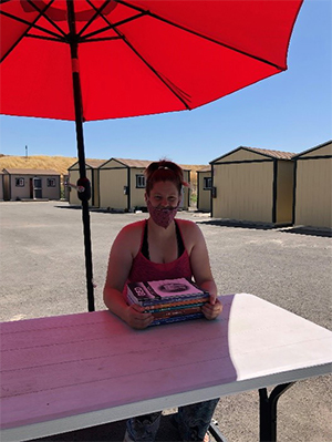 A woman sitting under a red umbrella at a Better Way picnic table